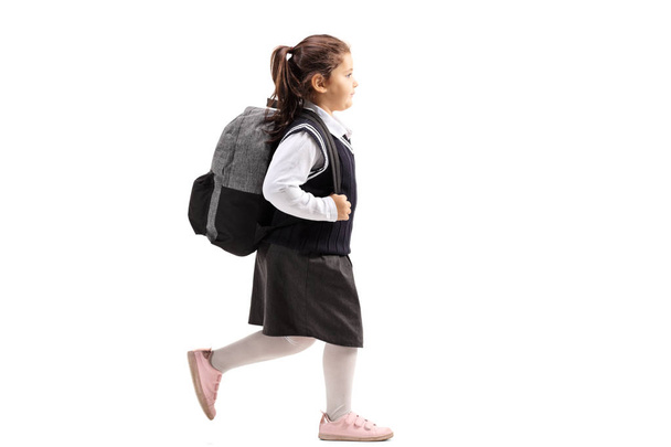 Full length profile of a schoolgirl with a backpack in a uniform walking isolated on white background - Fotó, kép