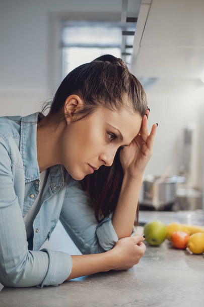 Vihainen tyttö päänsärky nojaten keittiön työtaso ja katselee alas
 - Valokuva, kuva