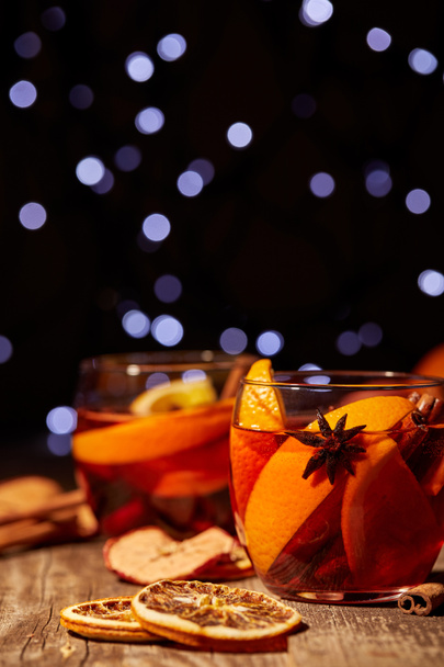 close up view of delicious hot mulled wine drinks and spices on wooden tabletop with defocused bokeh lights on background - Photo, Image
