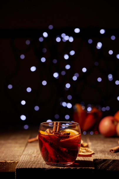 close up view of hot mulled wine drink with orange pieces and anise stars on wooden surface with bokeh lights on background - Fotoğraf, Görsel