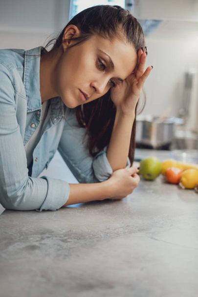Smutna dziewczyna z bólem głowy, opierając się na blat kuchenny i patrząc w dół - Zdjęcie, obraz
