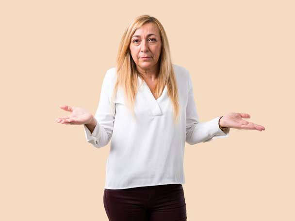 Middle age blonde woman with white shirt unhappy and frustrated with something because not understand something. Negative facial expression on isolated ocher background - Photo, Image