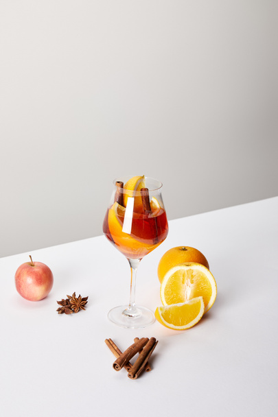 close up view of mulled wine in glass and ingredients arranged around on white tabletop on grey backdrop - Фото, зображення