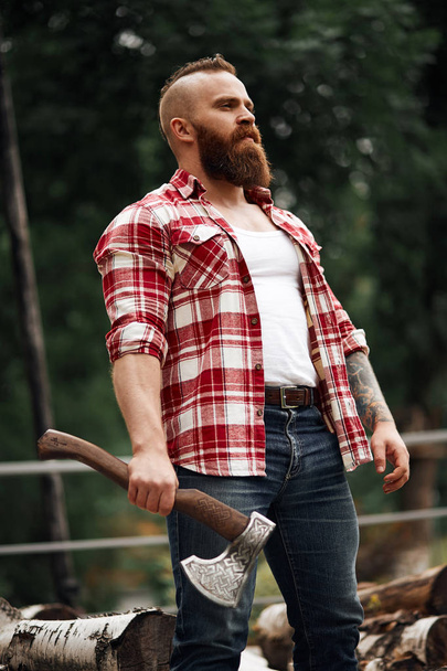 bearded lumberjack worker standing in forest with axe - Photo, image
