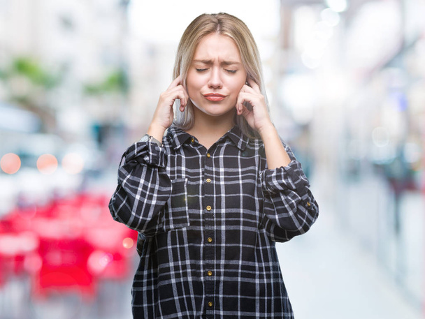 Young blonde woman over isolated background covering ears with fingers with annoyed expression for the noise of loud music. Deaf concept. - Photo, image