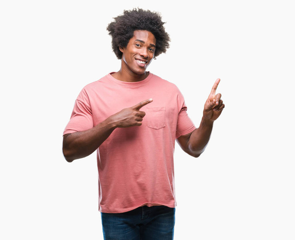 Αφρο αμερικανικό άνθρωπος πέρα από το απομονωμένο υπόβαθρο χαμογελώντας και εξετάζοντας τη φωτογραφική μηχανή κατάδειξης με δύο χέρια και τα δάχτυλα στο πλάι. - Φωτογραφία, εικόνα