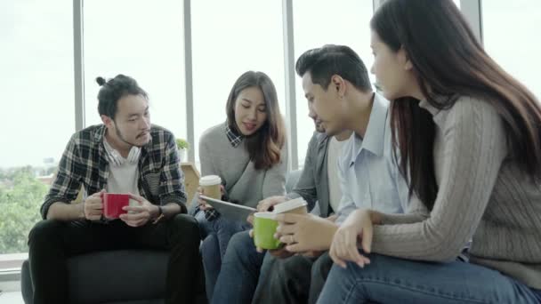 Multiethnic creative team diversity of young people group team holding coffee cups and discussing ideas meeting with tablet sitting on the couch at office. Coffee break time at creative office. - Footage, Video