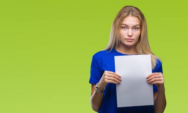 Young caucasian woman holding blank paper sheet over isolated background with a confident expression on smart face thinking serious - Photo, Image