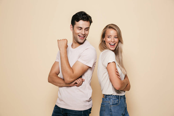 Portrait of a smiling young couple standing together over beige background, looking at each other - Foto, Imagen