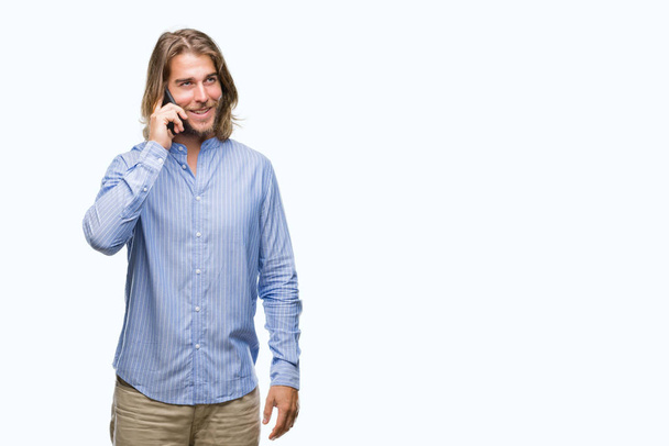 Young handsome man with long hair over isolated background talking on the phone with a happy face standing and smiling with a confident smile showing teeth - Foto, imagen
