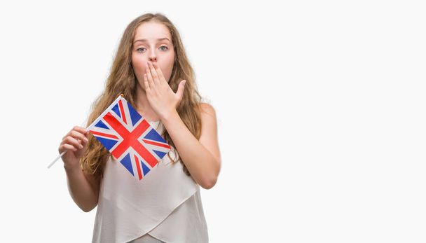 Mladá blond žena držící vlajka Velká Británie kryt ústa rukou šokován studem za chybu, výraz strachu, strach v tichosti, tajné koncept - Fotografie, Obrázek