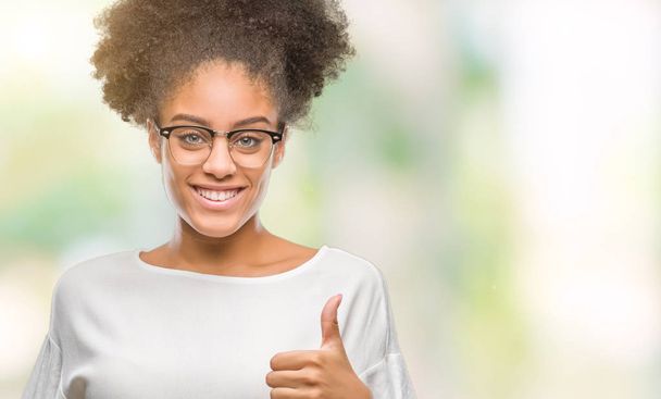 Young afro american woman wearing glasses over isolated background doing happy thumbs up gesture with hand. Approving expression looking at the camera with showing success. - Photo, Image