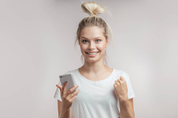 Happy woman with smart phone in one hand and looking at camera, isolated. - Photo, image