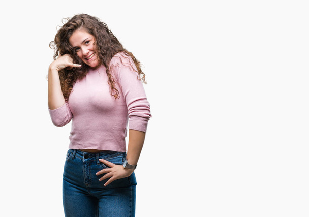 Beautiful brunette curly hair young girl wearing pink sweater over isolated background smiling doing phone gesture with hand and fingers like talking on the telephone. Communicating concepts. - Photo, Image