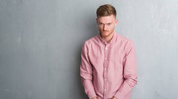 junger rothaariger Mann über der grauen Grunge-Wand in rosa Hemd skeptisch und nervös, die Stirn runzelnd ob des Problems. Negative Person. - Foto, Bild