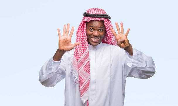 Νεαρός Αραβικά Αφρικής άνδρας φορώντας παραδοσιακές keffiyeh πέρα από το απομονωμένο υπόβαθρο δείχνει και δείχνει προς τα επάνω με τα δάχτυλα αριθμός εννέα, ενώ χαμογελώντας αυτοπεποίθηση και χαρούμενοι. - Φωτογραφία, εικόνα