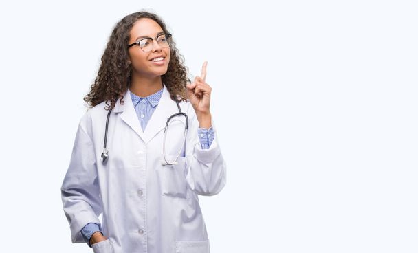 Young hispanic doctor woman surprised with an idea or question pointing finger with happy face, number one - Φωτογραφία, εικόνα