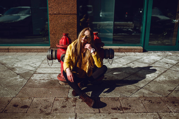 A young European woman, traveling, with long blond hair, wearing a yellow jacket, yellow sunglasses walking down the city center street, street shooting. Even light. - Φωτογραφία, εικόνα