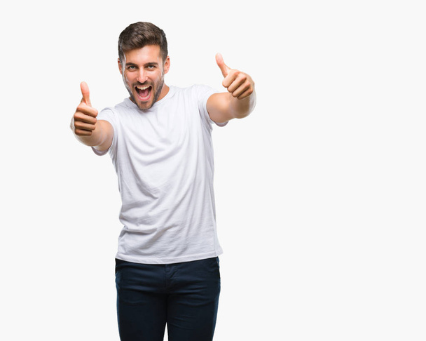 Young handsome man over isolated background approving doing positive gesture with hand, thumbs up smiling and happy for success. Looking at the camera, winner gesture. - Photo, Image