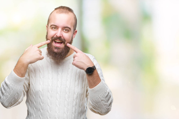 Giovane uomo hipster caucasico indossa maglione invernale su sfondo isolato sorridente fiducioso mostrando e indicando con i denti delle dita e della bocca. Concetto sanitario
. - Foto, immagini