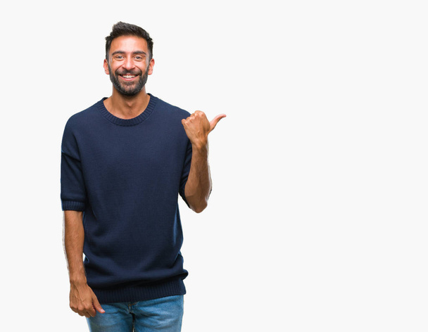 Adult hispanic man over isolated background smiling with happy face looking and pointing to the side with thumb up. - Foto, afbeelding