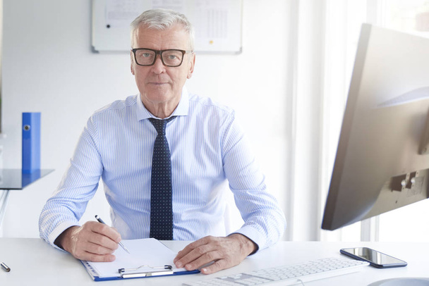 Shot of financial professional man doing some paperwork while sitting at office desk. - Fotoğraf, Görsel