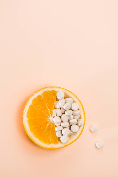 Tablets with vitamins in an orange slice on a beige background. - Foto, afbeelding