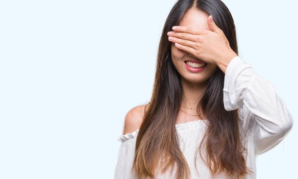 Jovem mulher asiática sobre fundo isolado sorrindo e rindo com a mão no rosto cobrindo os olhos para surpresa. Conceito cego
. - Foto, Imagem