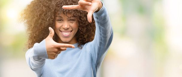 アフリカ系アメリカ人の女性の手で作るフレームと幸せそうな顔で指を笑顔のセーターを着てします。創造性と写真のコンセプト. - 写真・画像
