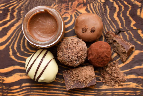 Handmade chocolate candies and jar of chocolate paste on wooden background. Top view - Photo, Image