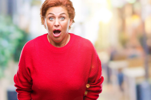 Στιβαρό και ανώτερος Καυκάσιος Κοκκινομάλλης γυναίκα φορώντας χειμώνα πουλόβερ πέρα από το απομονωμένο υπόβαθρο φοβάται και σοκαρισμένος με έκφραση έκπληξη, φόβο και ενθουσιασμένος για το πρόσωπό. - Φωτογραφία, εικόνα
