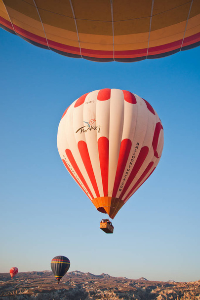 Goreme, Turkije - 4 April 2012: hete lucht ballonnen voor toeristen vliegen over rotsformaties bij zonsopgang in de vallei van Cappadocië. - Foto, afbeelding
