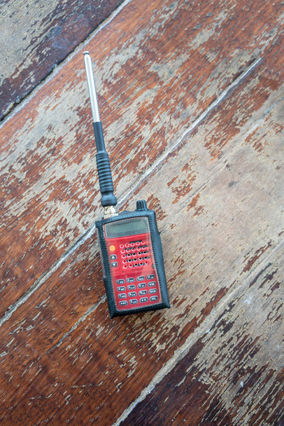 Transceptor de radio. Dispositivo portátil rectángulo rojo con botones amarillos y negros y antena plateada sobre fondo de madera
. - Foto, Imagen