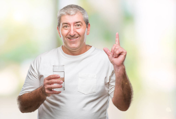 Hombre mayor guapo bebiendo un vaso de agua sobre un fondo aislado sorprendido con una idea o pregunta apuntando con el dedo con la cara feliz, número uno
 - Foto, imagen