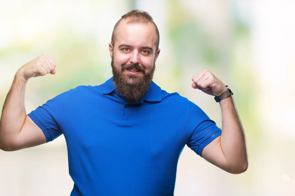 Joven hombre hipster caucásico con camisa azul sobre fondo aislado mostrando los músculos de los brazos sonriendo orgulloso. Concepto Fitness
. - Foto, imagen