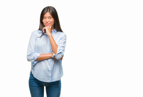 Молодая азиатская деловая женщина на изолированном фоне, уверенно смотрящая в камеру со скрещенными руками и поднятой на подбородок рукой. Мысли позитивно
. - Фото, изображение