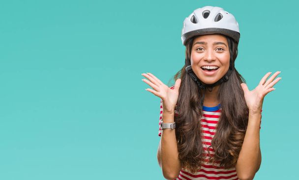 Joven ciclista árabe mujer con casco de seguridad sobre un fondo aislado celebrando loco y sorprendido por el éxito con los brazos levantados y los ojos abiertos gritando emocionados. Concepto ganador
 - Foto, imagen