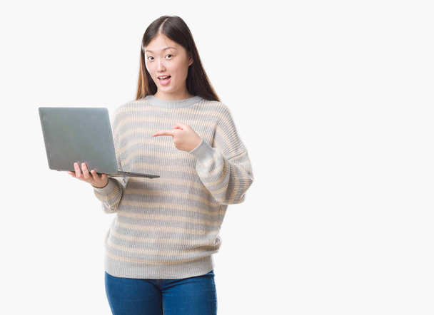 Joven mujer china sobre fondo aislado utilizando computadora portátil muy feliz señalando con la mano y el dedo
 - Foto, imagen
