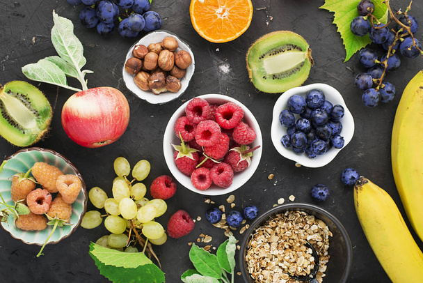 Ingredients for healthy breakfast meals: raspberries, blueberries, nuts, orange, bananas, grapes blue, green apples kiwi Top View - Foto, Imagen