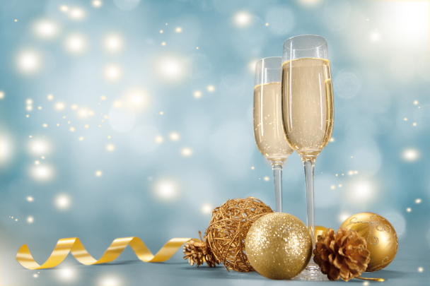 Két pohár pezsgőt és karácsonyi játékok egy bokeh alapon arany szalaggal díszített. - Fotó, kép