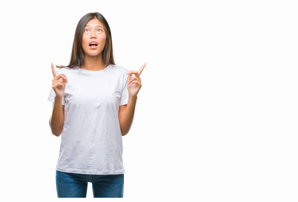 Young asian woman over isolated background amazed and surprised looking up and pointing with fingers and raised arms. - Photo, image