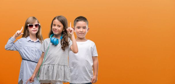 Group of boy and girls kids over orange background surprised with an idea or question pointing finger with happy face, number one - Photo, Image