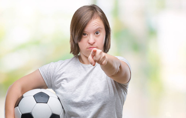 Mulher adulta jovem com síndrome de down segurando bola de futebol sobre fundo isolado apontando com o dedo para a câmera e para você, sinal de mão, gesto positivo e confiante da frente
 - Foto, Imagem