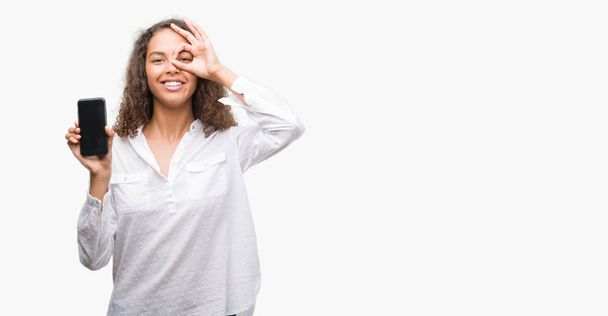 Giovane donna ispanica utilizzando smartphone con volto felice sorridente facendo ok segno con mano sugli occhi guardando attraverso le dita
 - Foto, immagini