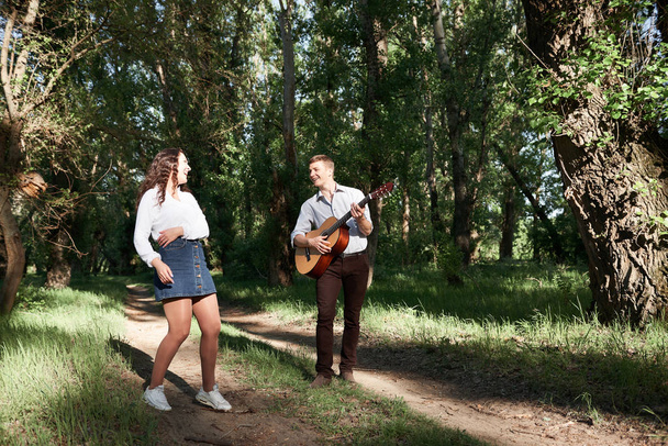 pareja joven caminando en el bosque, tocando la guitarra y bailando, naturaleza de verano, luz del sol brillante, sombras y hojas verdes, sentimientos románticos
 - Foto, imagen