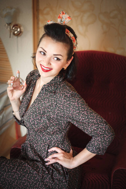 Girl with perfume. Closeup beautiful young woman pretty smiling pinup girl holding bottle of perfume and smelling aroma, retro vintage 50's hairstyle - 写真・画像