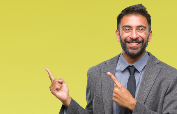 Взрослый латиноамериканец на изолированном фоне улыбается и смотрит в камеру, указывая двумя руками и пальцами в сторону
. - Фото, изображение