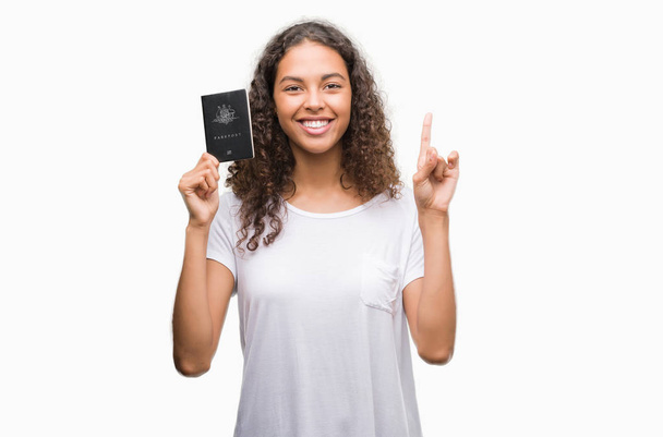 Mujer hispana joven con pasaporte de Australia sorprendida con una idea o pregunta apuntando con el dedo con la cara feliz, número uno
 - Foto, Imagen