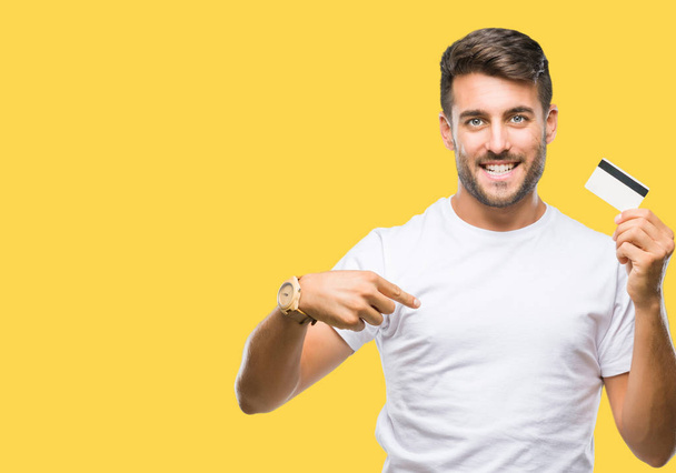 Young handsome man holding credit card over isolated background with surprise face pointing finger to himself - Foto, imagen