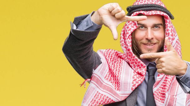 junger gut aussehender arabischer Mann mit langen Haaren, der Keffiyeh über isoliertem Hintergrund trägt und lächelnd einen Rahmen mit Händen und Fingern mit glücklichem Gesicht bildet. Kreativität und Fotografiekonzept. - Foto, Bild